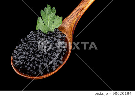 Close-up of a wooden spoon full of black caviar with a parsley leaf on a black background. Close-up of a wooden spoon full of black caviar with a parsley leaf on a black background. 90620194