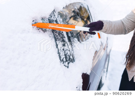Woman cleans car with a brush from snow after a blizzard 90620269