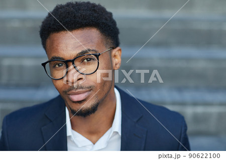 Portrait of content handsome young smart African-American man in eyeglasses sitting on staircase outdoors 90622100