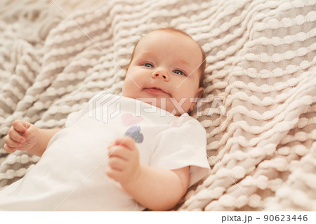 iling little newborn baby in white cotton bodysuit lying on bed and smiling at camera 90623446