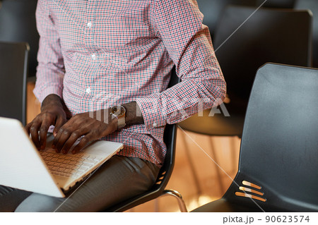 Close-up of unrecognizable Black man with wristwatch sitting on chair and composing business article on laptop 90623574
