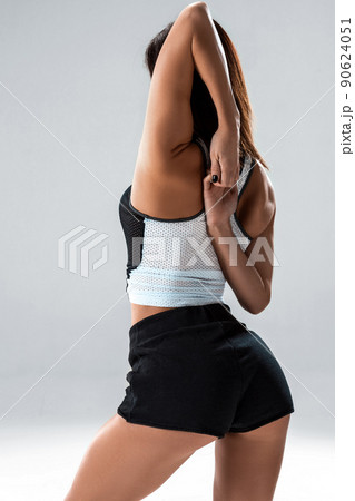 Slim and sport young woman posing and doing sport exercises standing with her back to the camera and stretching arms in studio isolated over gray background Slim and sport young woman posing and doing sport exercises standing with her back to the camera and stretching arms in studio isolated over gray background 90624051