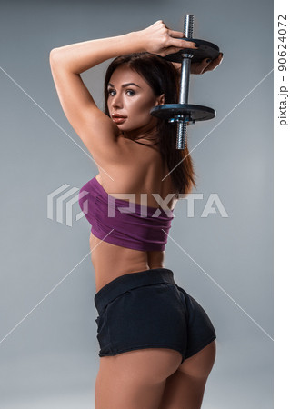 Studio portrait of a sporty young woman posing with dumbbell against a gray background. Close-up 90624072