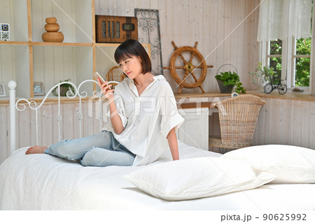 ベッドに座ってスマホを見る若い女性 90625992