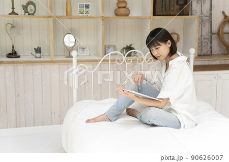 ベッドに座ってタブレットを見る若い女性 90626007