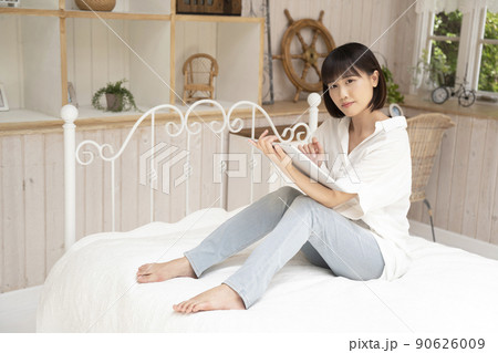 ベッドに座ってタブレットを見る若い女性 90626009
