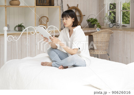 ベッドに座ってタブレットを見る若い女性 90626016