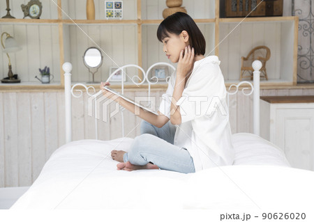 ベッドに座ってタブレットを見る若い女性 90626020