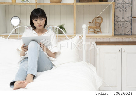 ベッドに座ってタブレットを見る若い女性 90626022