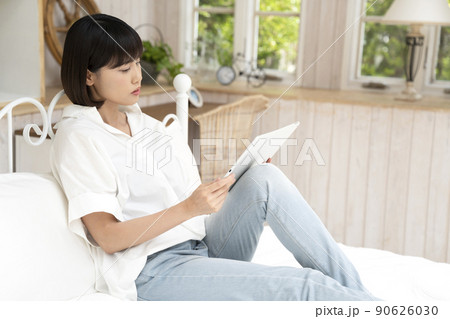 ベッドに座ってタブレットを見る若い女性 90626030