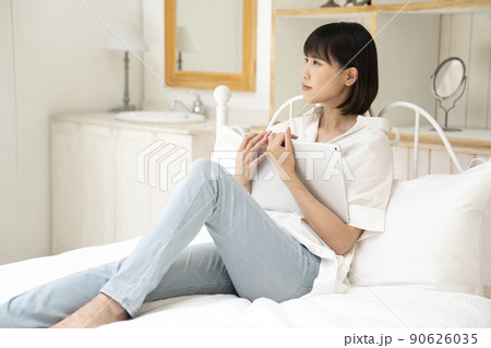 ベッドに座ってタブレットを見る若い女性 90626035