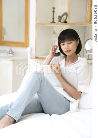 ベッドに座ってタブレットを見る若い女性 90626038