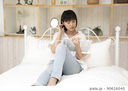 ベッドに座ってタブレットを見る若い女性 90626040