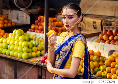 indian Caucasian woman in traditional dress.hindu model golden kundan jewelry set bindi earrings and nose ring piercing nath choosing fruits shopper in a supermarket fruit shop.exotic sale Kerala Goa indian Caucasian woman in traditional dress.hindu model golden kundan jewelry set bindi earrings and nose ring piercing nath choosing fruits shopper in a supermarket fruit shop.exotic sale Kerala Goa 90627829