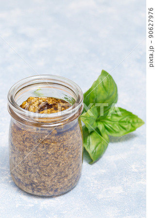 Basil green pesto sauce in glass jar, on light blue background, vertical, copy space 90627976