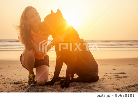 Blonde smiling young woman hugging her Cane Corso dog on the beach 90628181