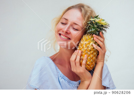 portrait of beautiful blond hair woman with blue eyes holding pineapple on white background.detox and allergy to tropical products portrait of beautiful blond hair woman with blue eyes holding pineapple on white background.detox and allergy to tropical products 90628206