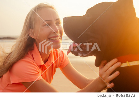 Blonde smiling young woman hugging her Cane Corso dog on the beach 90628272