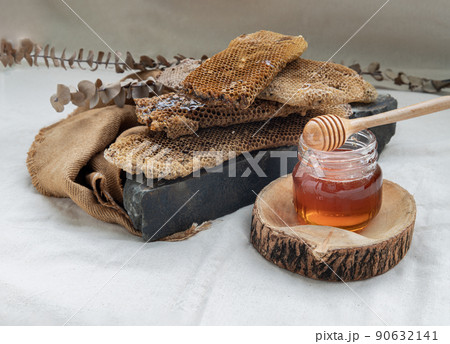 Delicious honey dripping from Fresh honeycombs on Glass jar with Wooden honey dipper stick on black rock. 90632141