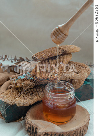 Delicious honey dripping from Wooden honey dipper stick into on Glass jar and Fresh honeycombs background. Delicious honey dripping from Wooden honey dipper stick into on Glass jar and Fresh honeycombs background. 90632561