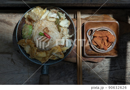 Stir fried rice vermicelli with pork dumplings, egg and vegetable in small steaming iron pot serve with crispy pork crackling or pork scratching. 90632626