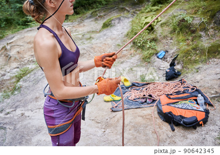 Close up of young female climber belaying leader during rock climbing outdoors, using rope, grigri, carabines and gloves. Concept of extreme sport and outdoor activity. 90642345