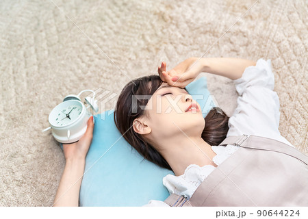 目覚まし時計を持った状態で2度寝する若い女性 90644224