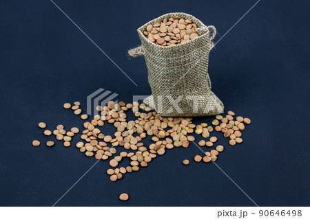 brown dried lentils in a burlap bag on black background 90646498