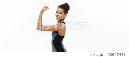 Healthy and Fitness concept - Portrait of young beautiful African American showing her strong muscle with confident cheerful facial expression. Isolated on white studio background. 90647481