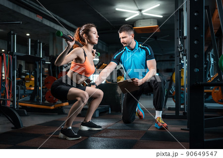 young female workout and exercising barbell squat in gym with personal trainer 90649547