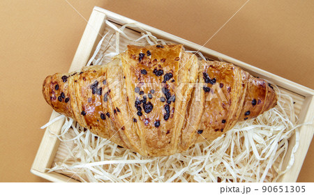 One regular fresh crispy whole grain croissant with chocolate filling on a brown or coffee background with copy space. Classic traditional freshly baked French dessert, pastries. Top view, flat lay. One regular fresh crispy whole grain croissant with chocolate filling on a brown or coffee background with copy space. Classic traditional freshly baked French dessert, pastries. Top view, flat lay. 90651305