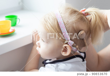 Mother fixing her daughter's cochlear implant hearing aid - deafness and diversity concept. Innovative technologies in treatment of deafness 90653670