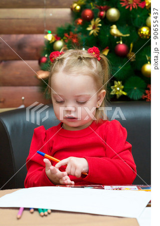 A little girl draws on the background of the Christmas tree. The concept of waiting for the holiday A little girl draws on the background of the Christmas tree. The concept of waiting for the holiday 90655437