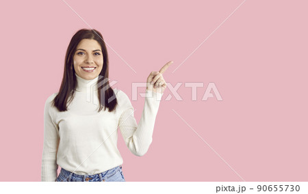 Happy young woman pointing her finger at something on pastel pink copy space background 90655730
