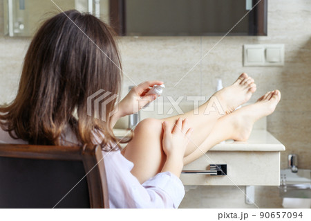 Woman in nightgown applying cream for protective and care dry skin legs sitting on armchair against mirror in bathroom. Woman in nightgown applying cream for protective and care dry skin legs sitting on armchair against mirror in bathroom. 90657094