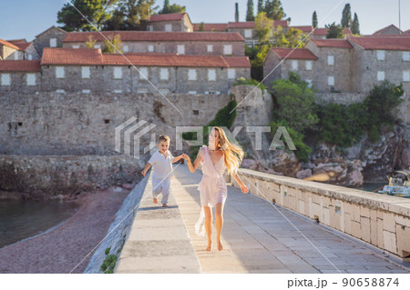 Mother and son tourists on background of beautiful view St. Stephen island, Sveti Stefan on the Budva Riviera, Budva, Montenegro. Travel to Montenegro concept Mother and son tourists on background of beautiful view St. Stephen island, Sveti Stefan on the Budva Riviera, Budva, Montenegro. Travel to Montenegro concept 90658874