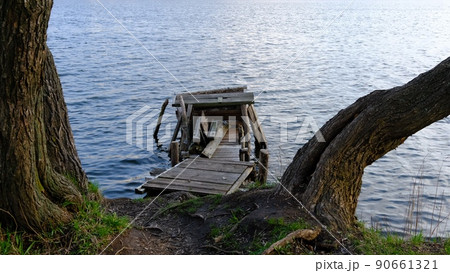 Autumn scene - lake and destroyed wooden pier. Old rotten wooden pier with missing planks with bench on a lake in the forest at autumn. 90661321
