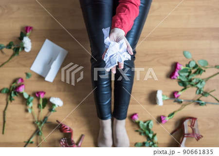 Unhappy woman sitting on the floor among scattered flowers and reading letter. Broken relationships in bad Valentine's day concept. Top view Unhappy woman sitting on the floor among scattered flowers and reading letter. Broken relationships in bad Valentine's day concept. Top view 90661835
