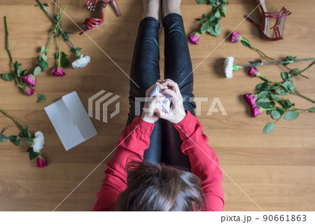 Unhappy woman sitting on the floor among scattered flowers and reading letter. breakup. bad Valentine's day. concept. Top view Unhappy woman sitting on the floor among scattered flowers and reading letter. breakup. bad Valentine's day. concept. Top view 90661863