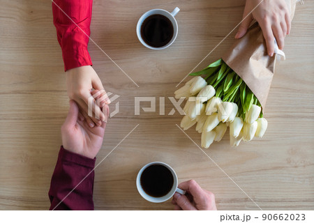 Valentines day.  Close-up of woman and man celebrating in restaurant. Boyfriend giving bouquet of tulips to girlfriend. love, romance, date. Flat lay 90662023