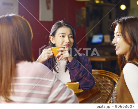 three happy beautiful young asian women sitting at table chatting talking in coffee shop or tea house three happy beautiful young asian women sitting at table chatting talking in coffee shop or tea house 90663607