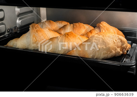Six baked homemade croissants on tray in electric oven at home 90663639