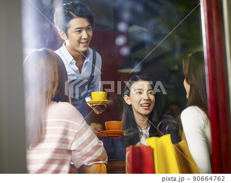 young asian waiter serving female customers in coffee shop, shot through window glass 90664762