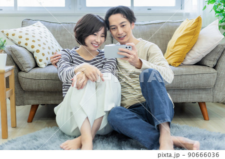 リビングでスマホを見ながらくつろぐカップル 90666036