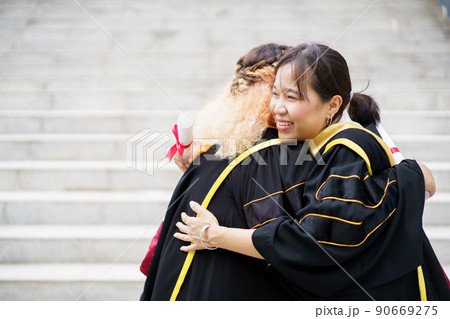 Happy Asian young women in the master degree gown showing a diploma in their hand close up. Portrait of confident college students in gown in the graduation ceremony. 90669275