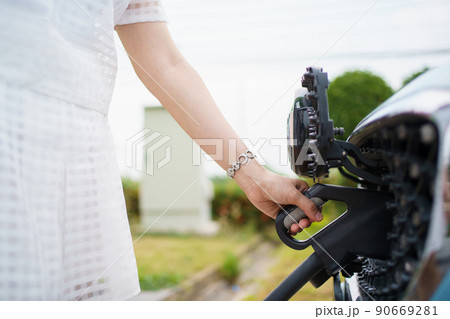 Unrecognizable Asian woman holding aa DC - CCS type 2 EV charging connector at EV charging station, woman preparing an EV - electric vehicle charging connector for recharge a vehicle. Unrecognizable Asian woman holding aa DC - CCS type 2 EV charging connector at EV charging station, woman preparing an EV - electric vehicle charging connector for recharge a vehicle. 90669281