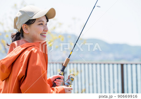 青空の下で趣味の釣りを楽しむ笑顔の若い女性 90669916