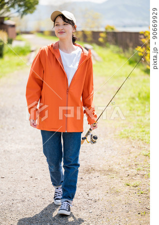 青空の下で楽しく歩きながら釣りポイントを探す笑顔の若い女性 90669929