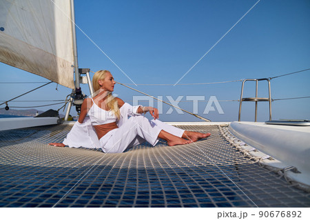 Beautiful young blond woman sitting on catamaran at sunny summer day Beautiful young blond woman sitting on catamaran at sunny summer day 90676892