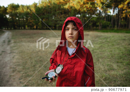 A boy in a red windbreaker against the backdrop of a forest with a compass in his hand. A boy in a red windbreaker against the backdrop of a forest with a compass in his hand. 90677971